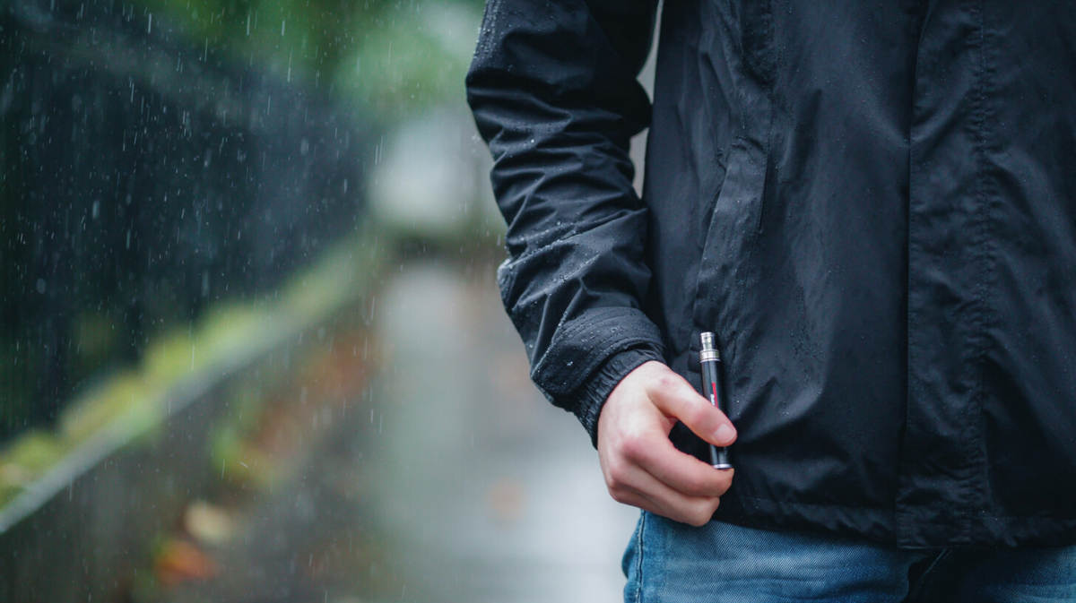Mężczyzna spacerujący w deszczu chowa do kieszeni e-papierosa